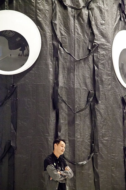 福島の汚染廃棄袋で作成した高さ6.9Ｍの彫刻《DADAモレ》2017年 の前に立つ岡本光博さん